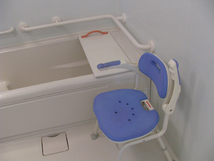 〔浴室〕跳ね上げ式の肘掛の付いたシャワーチェアと、移乗できるふたを使って入浴が可能です