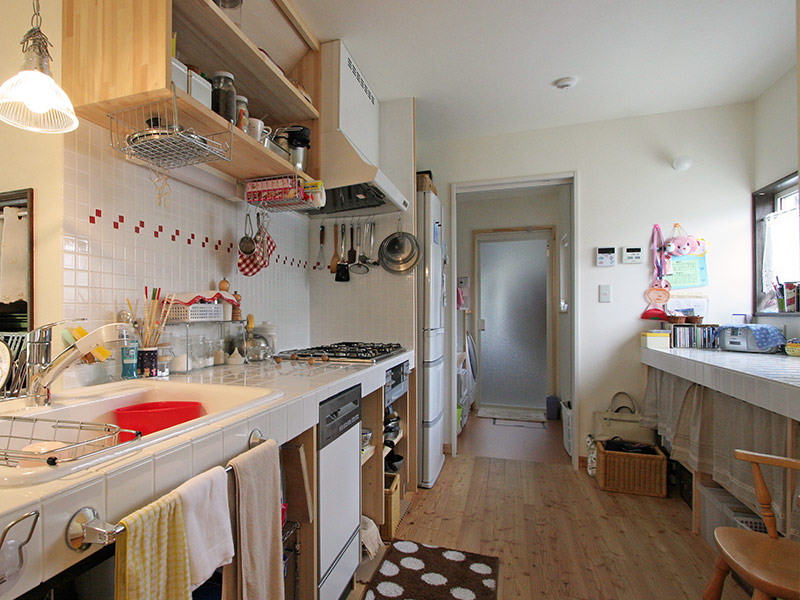 奥さまこだわりのキッチン。照明は百貨店で購入。収納は引き出しを使わずカフェカーテンで低コストに済ませ、レンジフードにS字フックで調理道具をぶら下げるなど、合理的に考えた