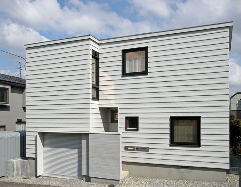 敷地にある高低差を生かして車庫をビルトイン。外装材に凸凹ある材料を使用し、シャープで立体的に仕上がった
